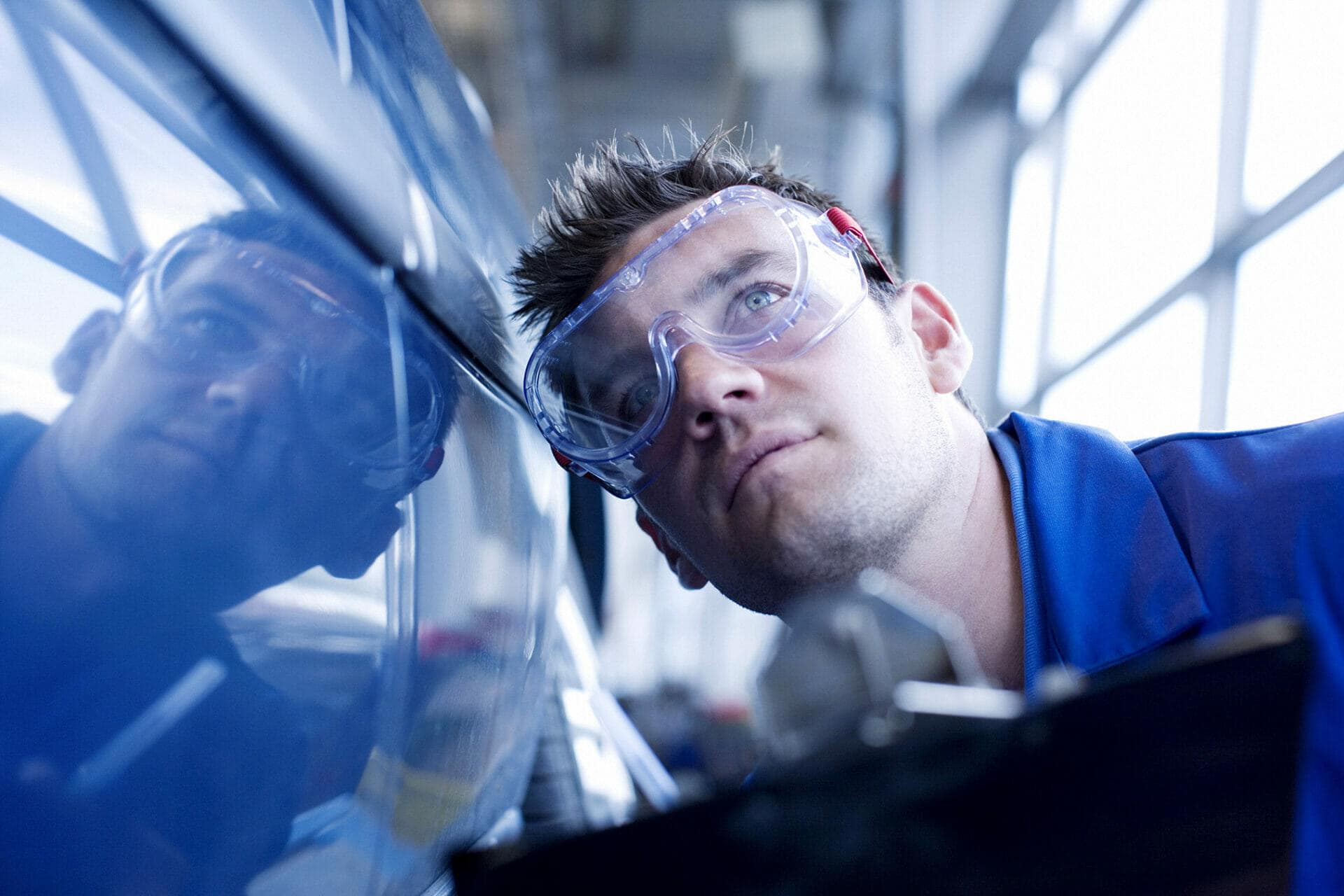 A mechanic is looking at the side of a blue car.