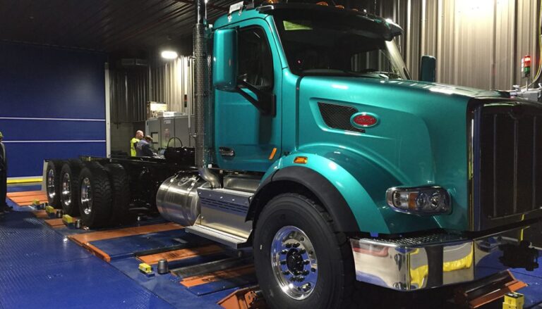 A green semi truck is being worked on in a garage.