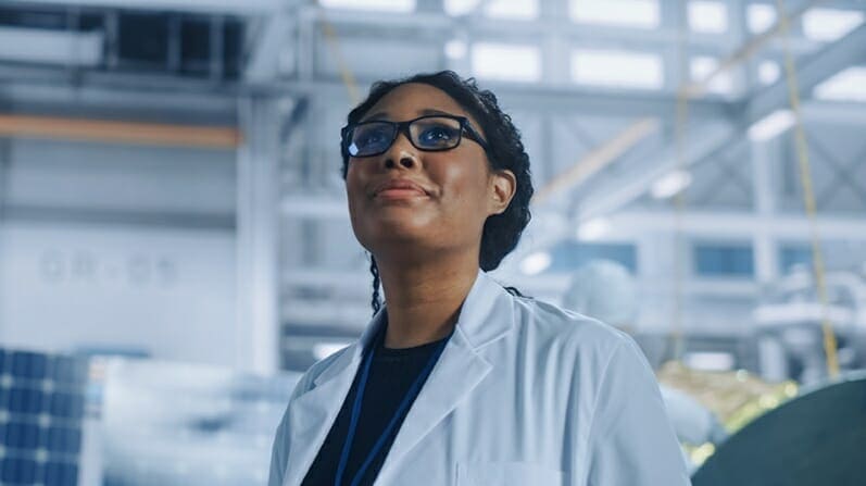 A woman in a lab coat standing in front of solar panels.