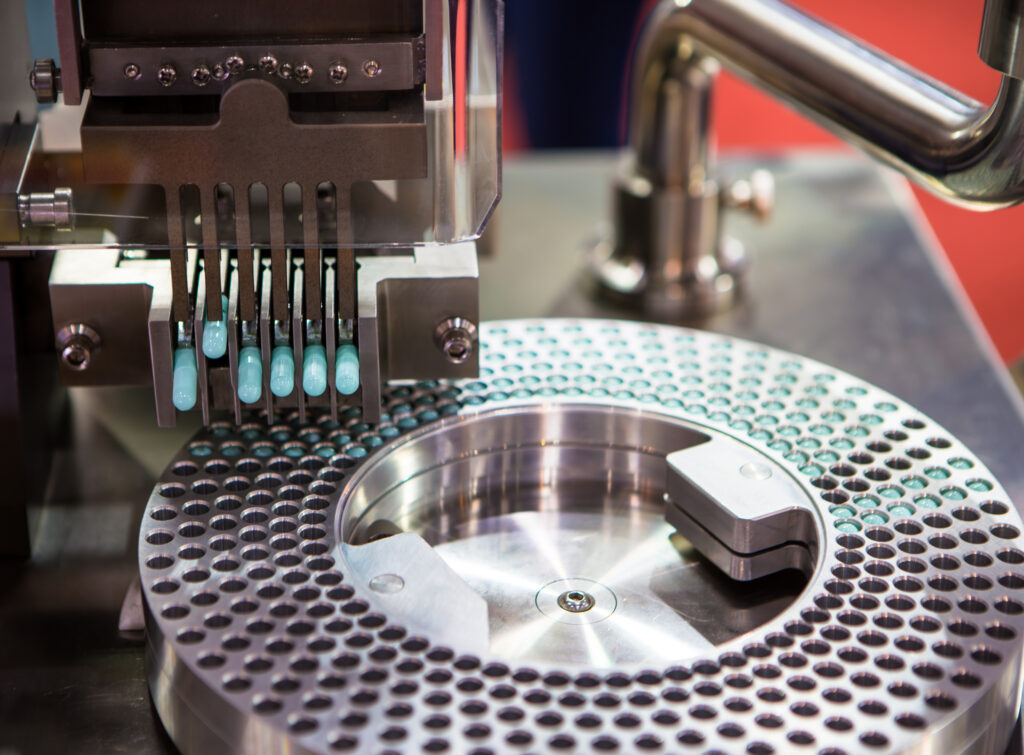 A pharmaceutical machine fills capsules on a metal rotating table with multiple small cavities.